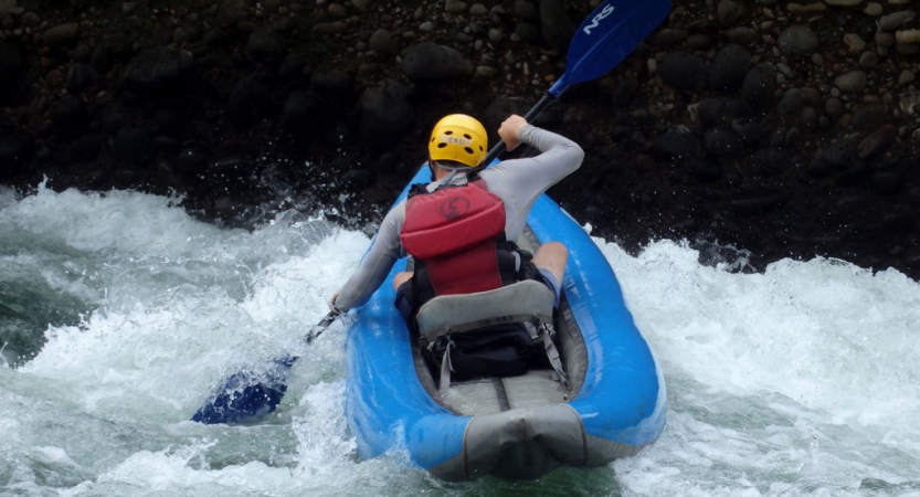 A person wearing safety gear paddles a watercraft through whitewater